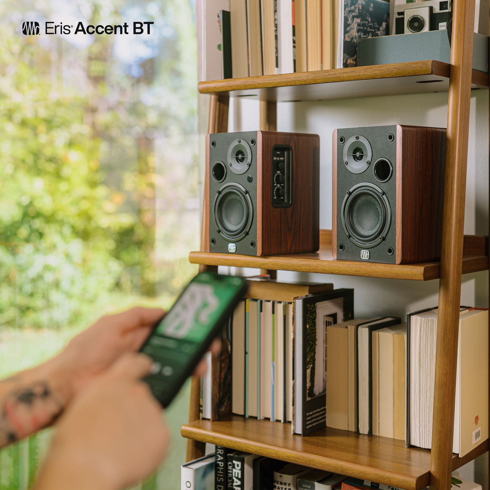 Kitaplık rafında Eris Accent BT çifti ve telefondan Bluetooth ile müzik oynatan kullanıcı